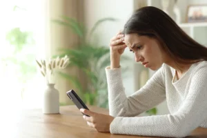 Frau schaut verzweifelt aufs Smartphone.
